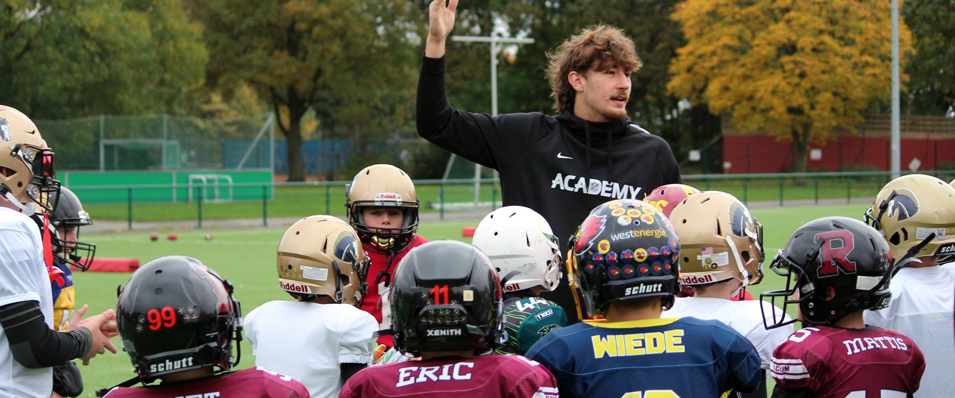 Coach erklärt Jugendlichen in Football-Ausrüstung eine Übung beim YFG American Football Camp